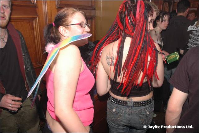 Two people from behind, one with long red dreadlocks and one with rainbow wings and pink top