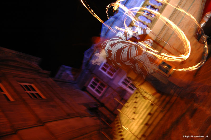 Fire poi trails and a tilted view of stone buildings at night
