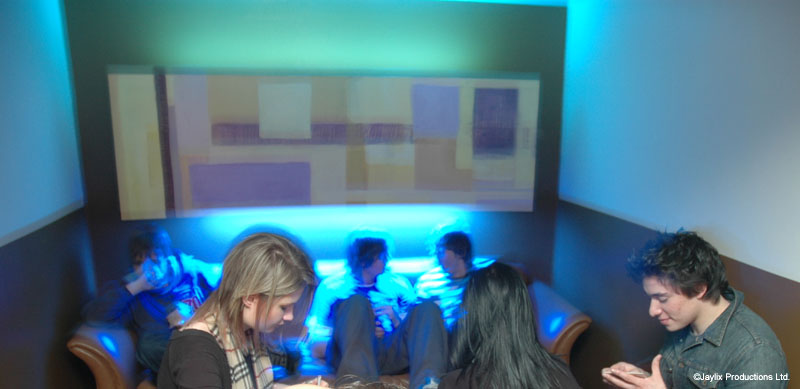 A few people sit on seats in a booth lit by blue light in a bar