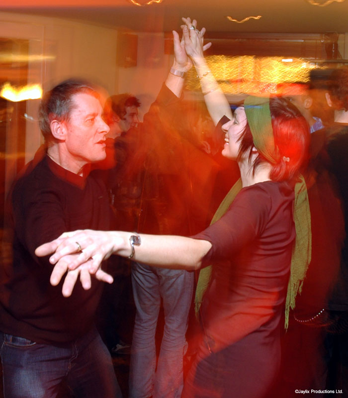 A man in dark clothes and a woman with a green scarf dance together, blurred with motion