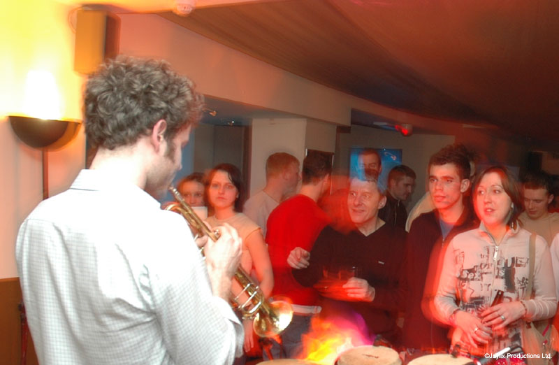 A man in a white shirt plays a trumpet while a crowd looks on behind drums