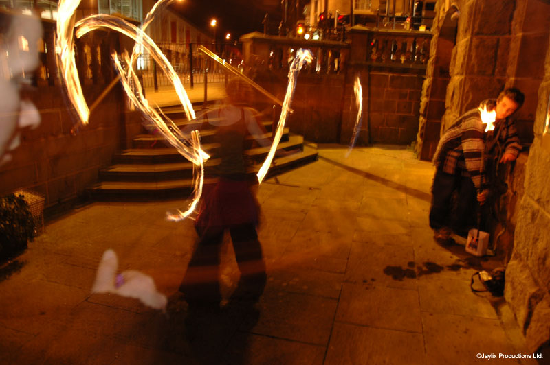 Blurred fire poi trails on stone steps at night, with a seated person on the right