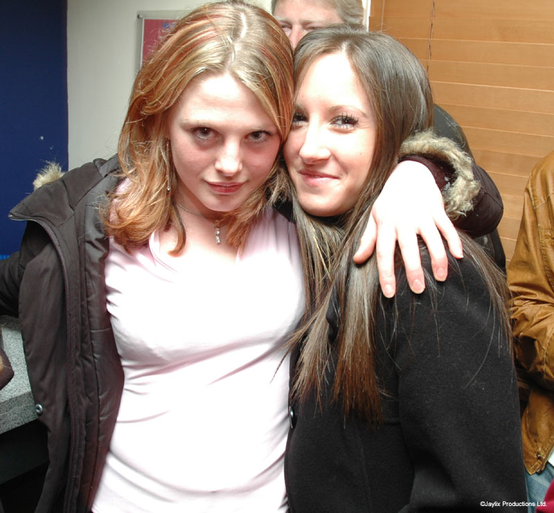 Two young women in coats hug and look at the camera