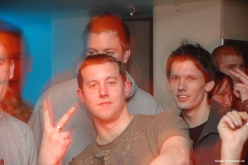 Three men in a busy bar, one in front making a peace sign, in blue and orange light