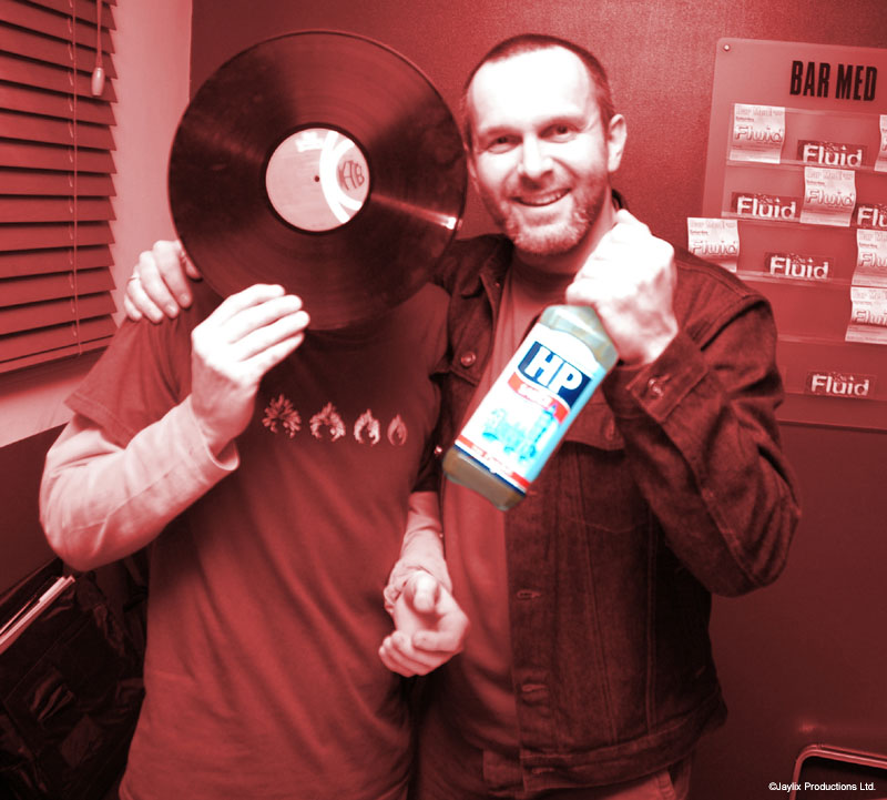 A man holding a bottle of HP sauce stands beside a person holding a vinyl record in front of their face, red-toned
