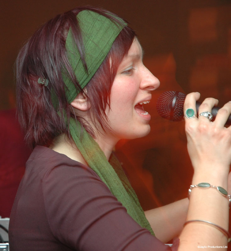 A woman with a green headscarf sings into a microphone