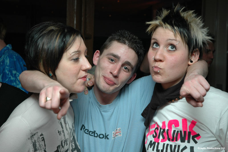 Three people pose close together with arms around each other, one in a light blue Reebok T-shirt