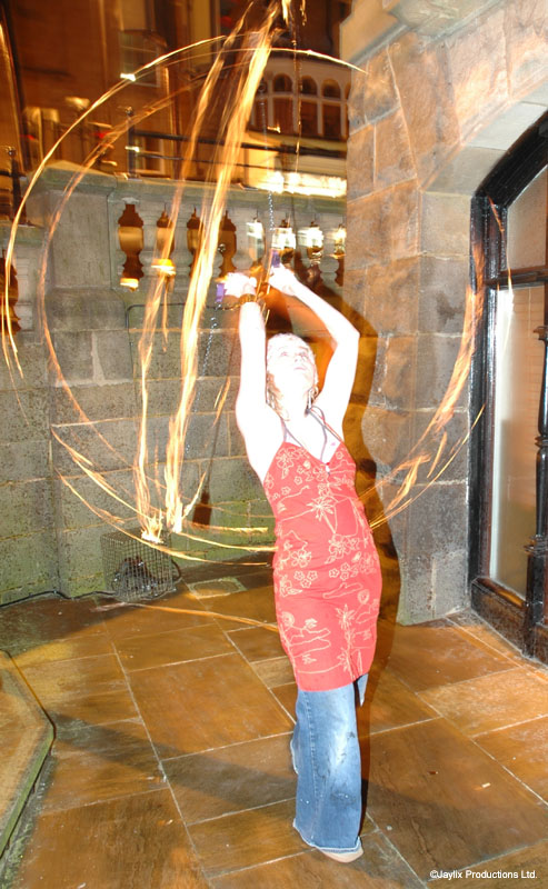 A person in a red dress spins fire in large circles on a stone terrace at night