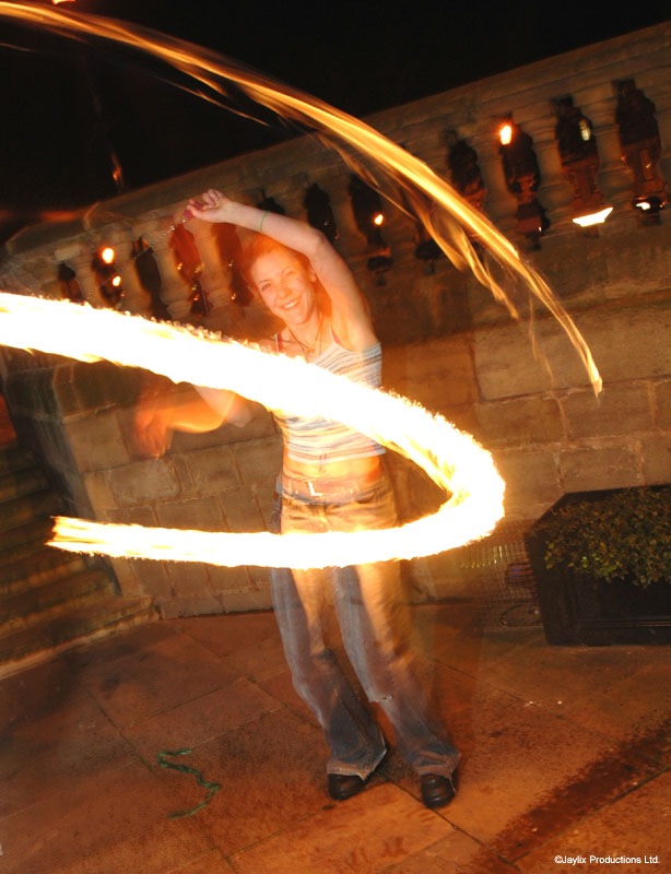 A person spins a ring of fire around their body on a stone terrace at night