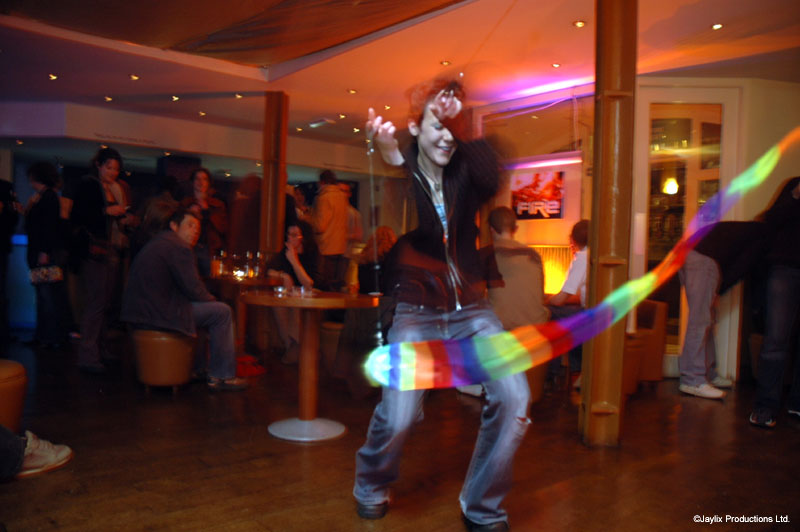 A person swings a rainbow-coloured ribbon in a bar, with people seated in the background
