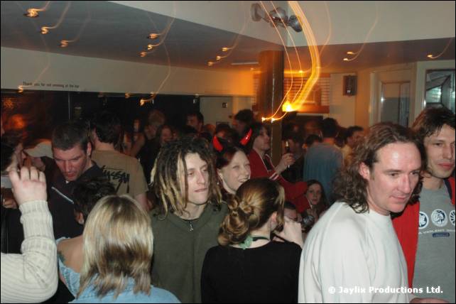 A crowded bar with people dancing, including a man with dreadlocks and a man in a white top