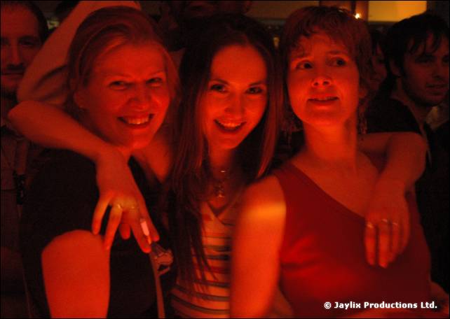 Three women with arms around each other smile in red lighting