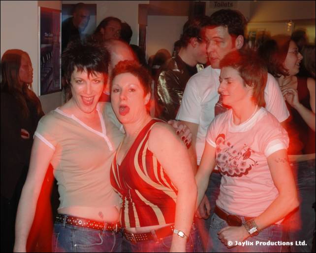 Three women pose with open mouths in a bar, with a man behind them