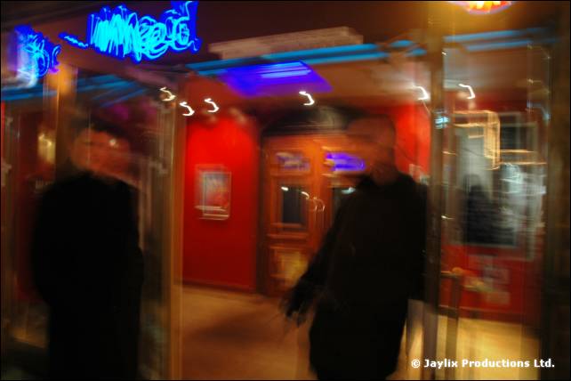 Blurred figures in a doorway under a blue neon sign at night, shot with a long exposure