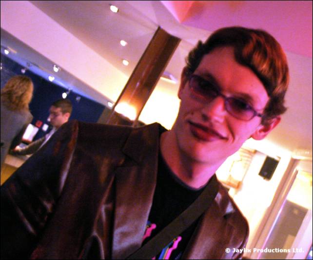 A man in sunglasses and a dark jacket looks at the camera in a brightly lit bar
