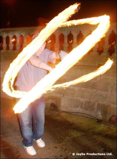 A person in a grey top spins fire in front of a stone balustrade at night
