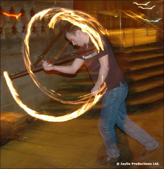 A person leans over while swinging a fire staff, with trails looping around them on stone steps