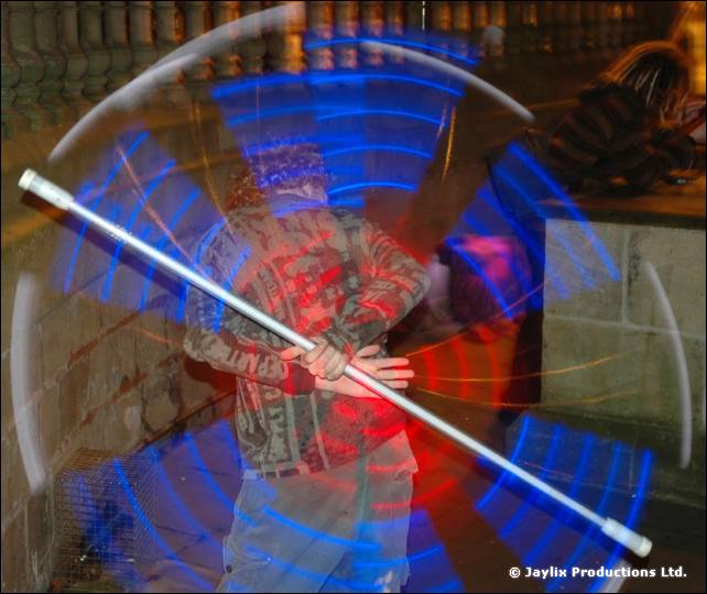A person swings a white staff with glowing blue and red light trails around them at night