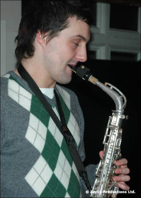 A man in a green and white argyle jumper plays a saxophone