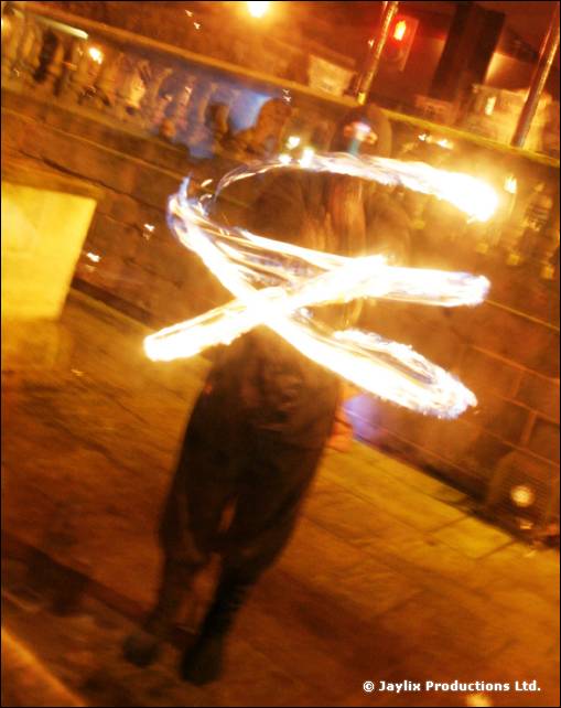 A blurred figure spins fire poi that cross in front of them on a street at night
