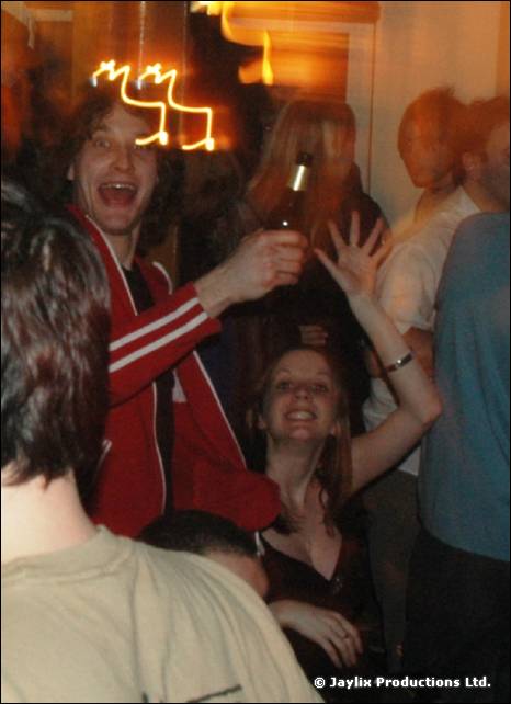 A man in a red striped jacket laughs with his mouth open in a crowd, with light streaks above him