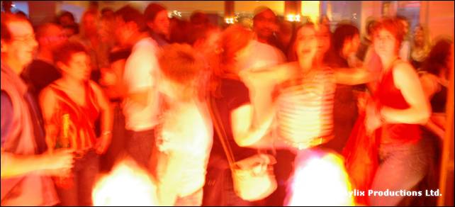 Blurred people dance in a crowded bar lit orange and red
