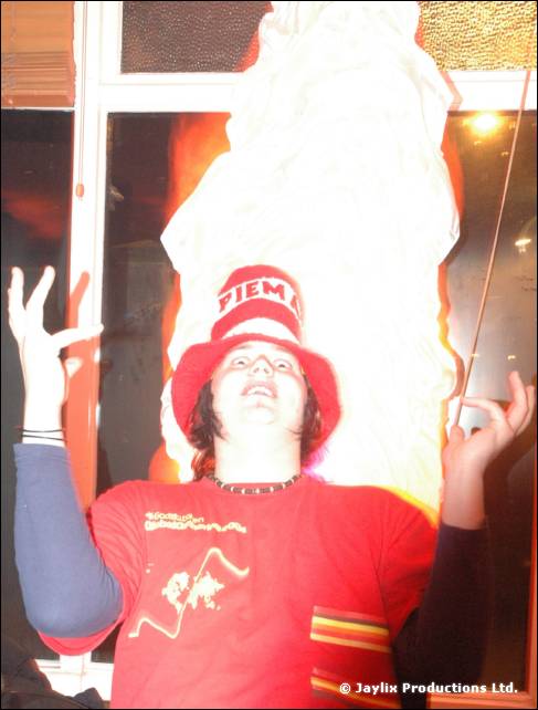 A person in a red Spanish-themed bucket hat and red T-shirt raises both hands in front of a glowing white form