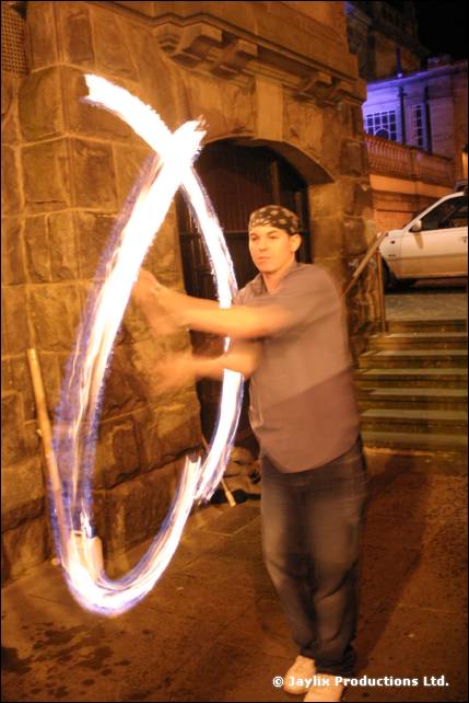 A person in a bandana spins a hoop of fire in front of a stone archway at night