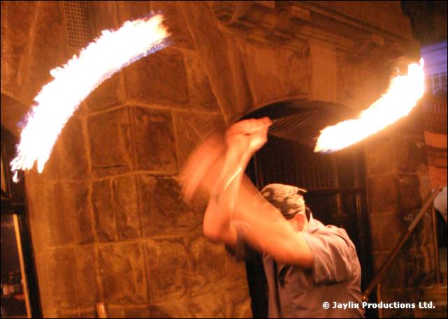 A person in a cap swings two flaming props in front of a stone archway at night