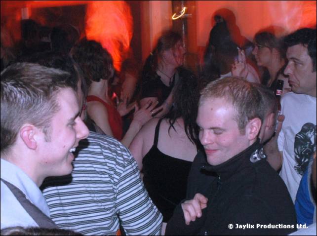 Men in striped tops smile and dance in a crowded bar, with other people behind