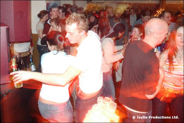 A man in a white shirt dances with a woman in a white top in a packed bar