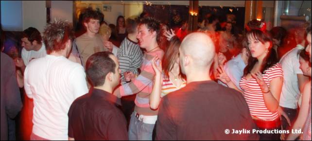 A crowd dances in a bar, including a woman in a red striped top and a bald man
