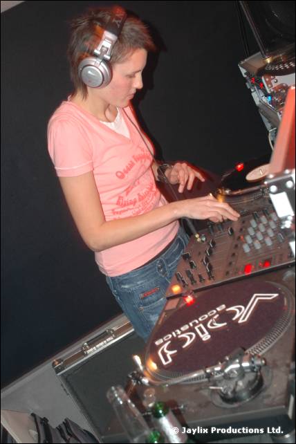 A DJ in a pink T-shirt and headphones mixes at turntables with a Void Acoustics platter