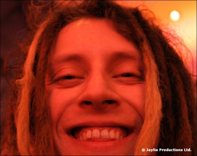 A close-up of a smiling person with long dreadlocks, lit orange