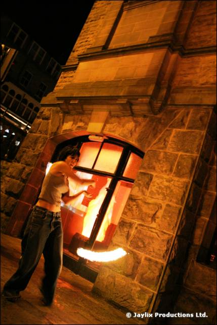 A person stands at an arched window of a stone building, with a flame glowing inside