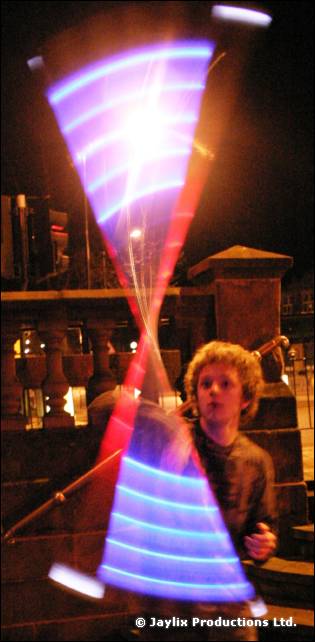 A child stands behind twisting blue and purple light trails from spinning poi at night