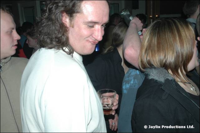 A smiling man with curly hair in a white top looks down, with a woman in a dark jacket beside him