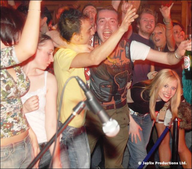 A crowd dances close to a microphone stand, arms raised, one person smiling at the camera