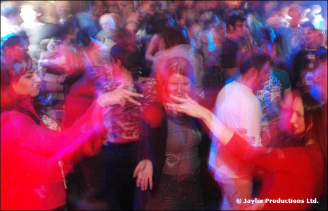 A packed dance floor blurred with movement, people in red tops dancing with their hands raised