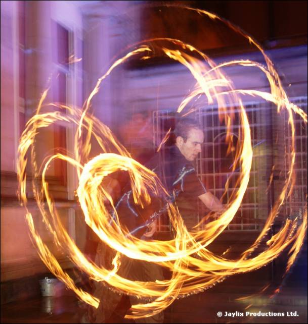 A person spins fire poi creating overlapping circles of flame in front of a window