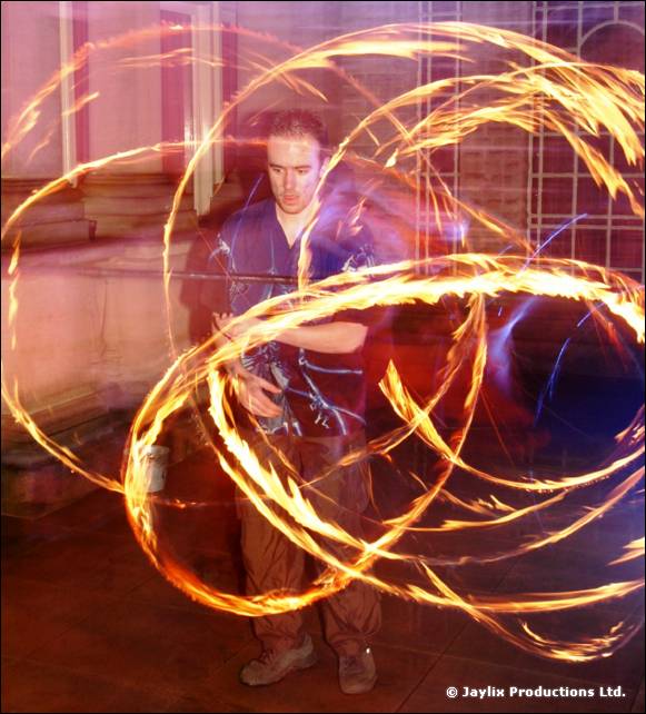 A person spins fire poi in overlapping loops in front of tall windows