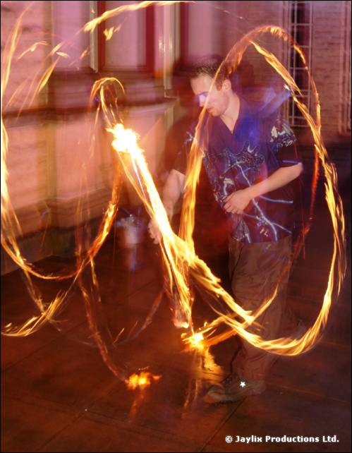 A person spins fire in long loops outside a stone building at night