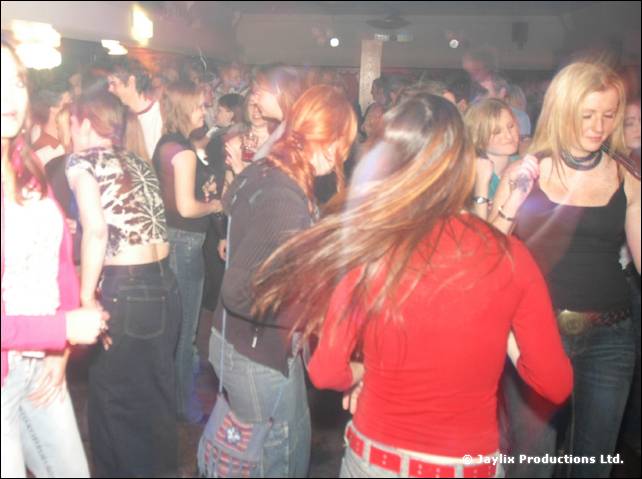 A crowd dances in a club, a person in a red top with long hair in the foreground