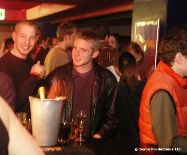 Two smiling people at a crowded bar, an ice bucket with a champagne bottle in the foreground