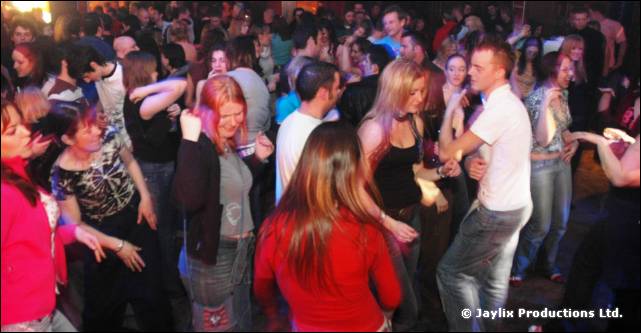 A crowded dance floor seen from behind, people dancing with arms raised