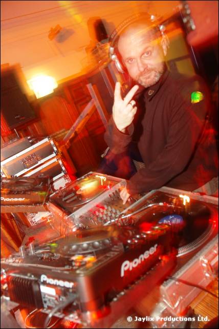 A bald DJ in headphones makes a peace sign at Pioneer decks
