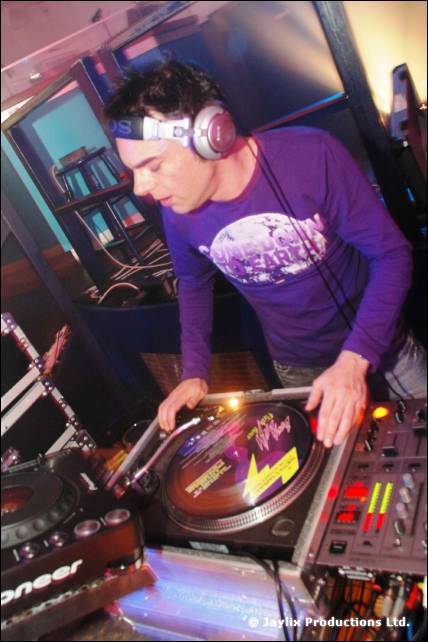 A DJ in a purple top and headphones mixes on Pioneer turntables
