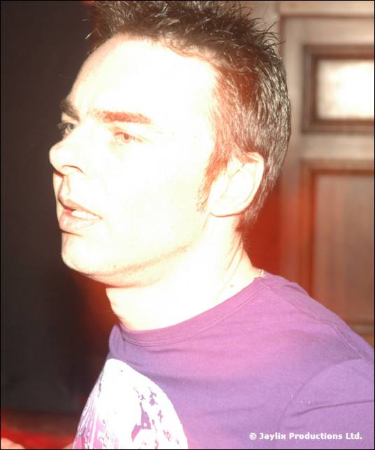 A close up of a person with short spiky hair in a purple t-shirt, looking to one side