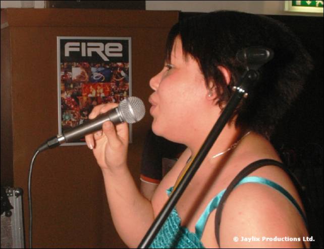 A person sings into a microphone in front of a FIRE poster on the wall