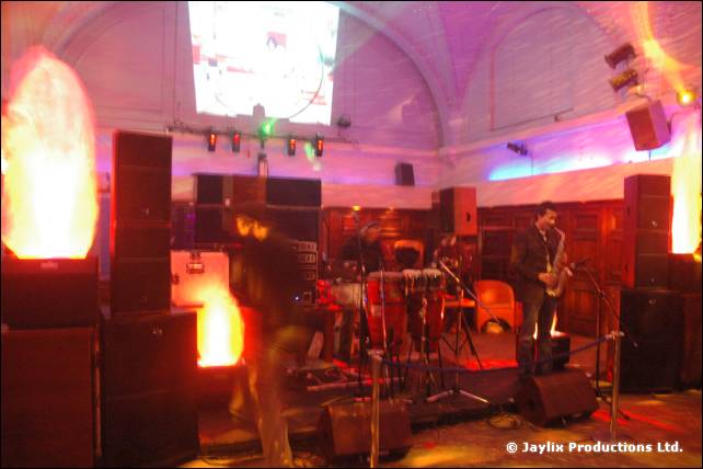 An empty stage with speakers, flame effects and a saxophonist standing at the back of the hall